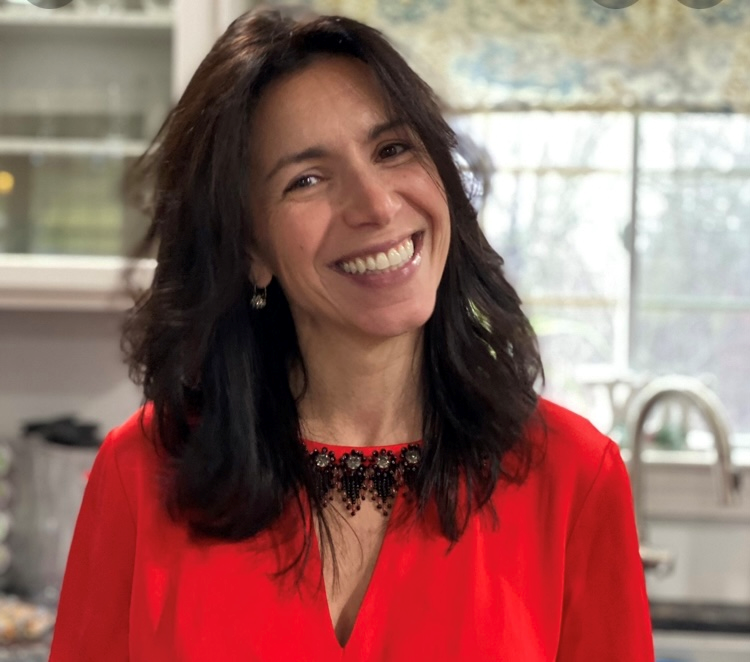 Nancy Murphy - white woman with medium-long brown hair, wearing a red-orange shirt, standing in a kitchen.