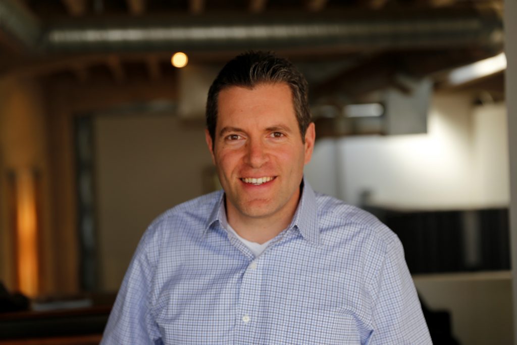 Barry Finegold - white man with short brown hair, wearing a blue collar shirt, standing in an office.